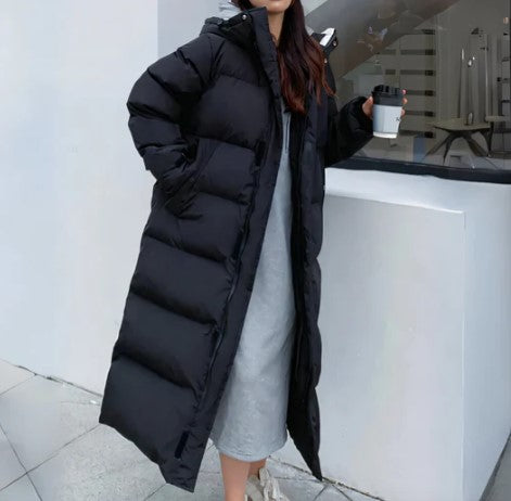 Femme portant un long manteau doudoune noir, tenant une tasse de café. Mode hiver, vêtement chaud, style urbain.