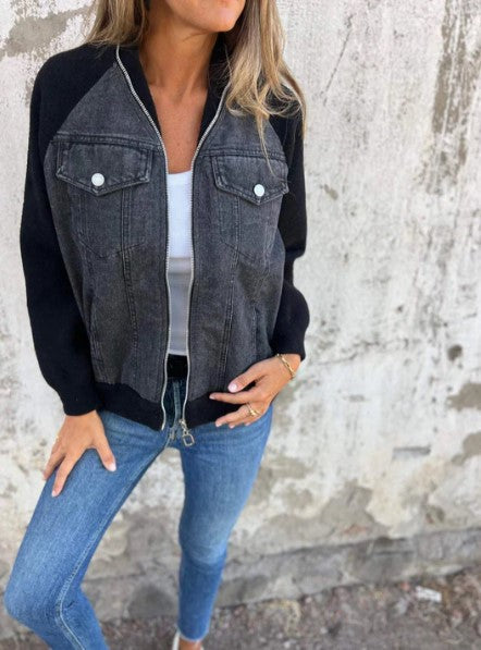 Femme portant une veste en jean noir avec manches longues, fermée par une fermeture éclair, sur un mur texturé. Mode décontractée, style urbain.