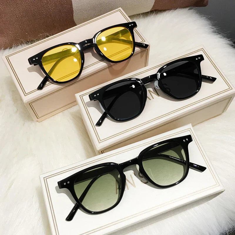 Lunettes de soleil élégantes avec montures noires et verres teintés jaune, noir et vert, posées sur des boîtes blanches sur fond de fourrure blanche.
