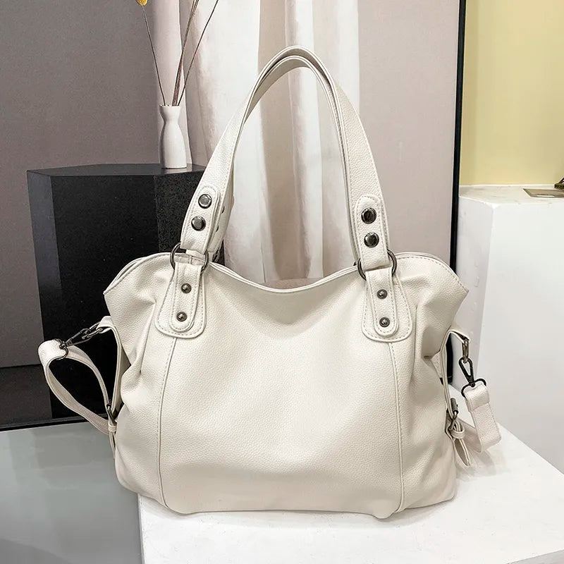 Sac à main en cuir blanc élégant avec poignées doubles et bandoulière amovible, posé sur une surface moderne. Accessoire mode femme chic.