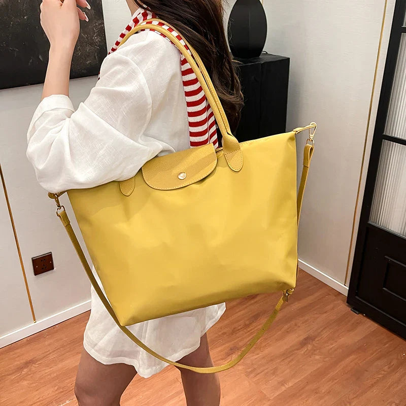 Femme portant un grand sac à main jaune en toile, avec bandoulière, sur fond intérieur moderne. Mode féminine, accessoire tendance, style décontracté.