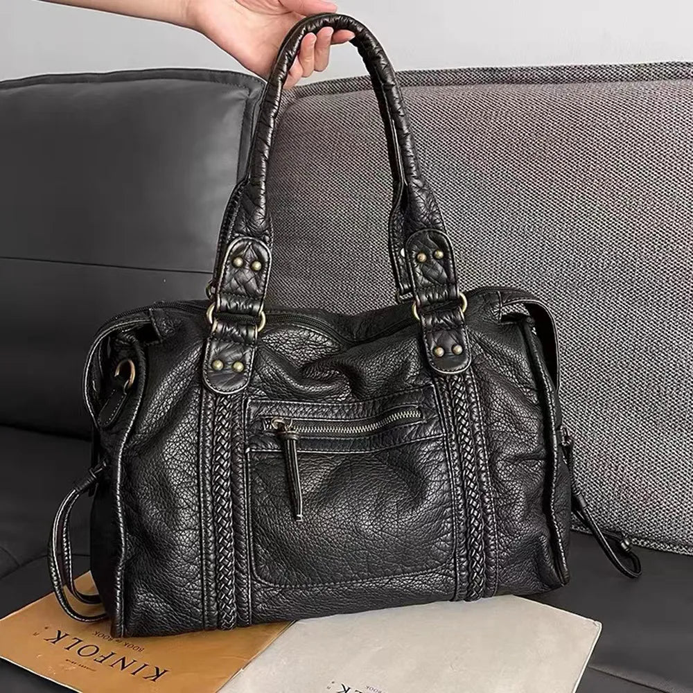 Sac à main en cuir noir texturé avec poignées robustes, posé sur un canapé gris. Design élégant, idéal pour la mode féminine et le quotidien.
