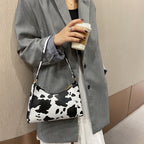 Femme en manteau gris tenant un sac à main motif vache et un café à emporter. Mode urbaine, accessoires tendance, style moderne.