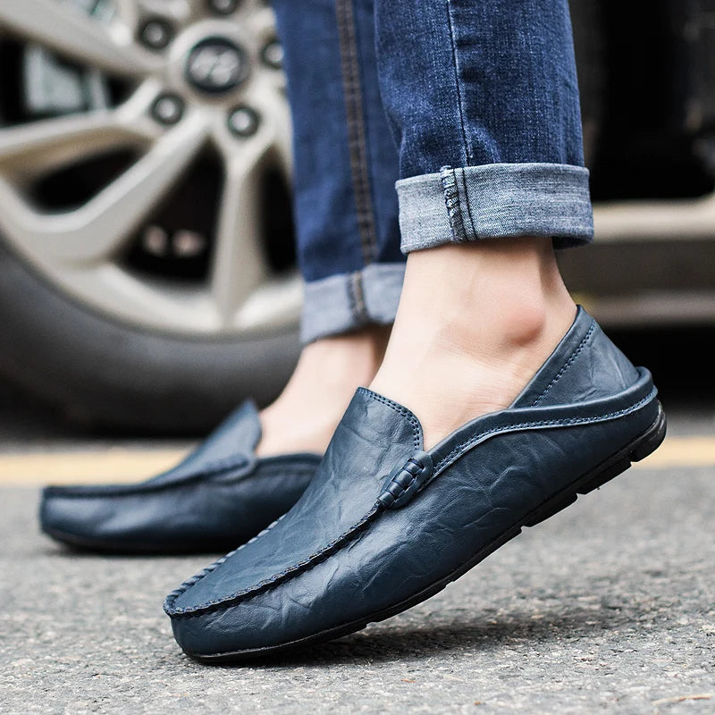 Chaussures mocassins en cuir bleu pour homme, portées avec un jean, sur fond de roue de voiture. Style décontracté et élégant.