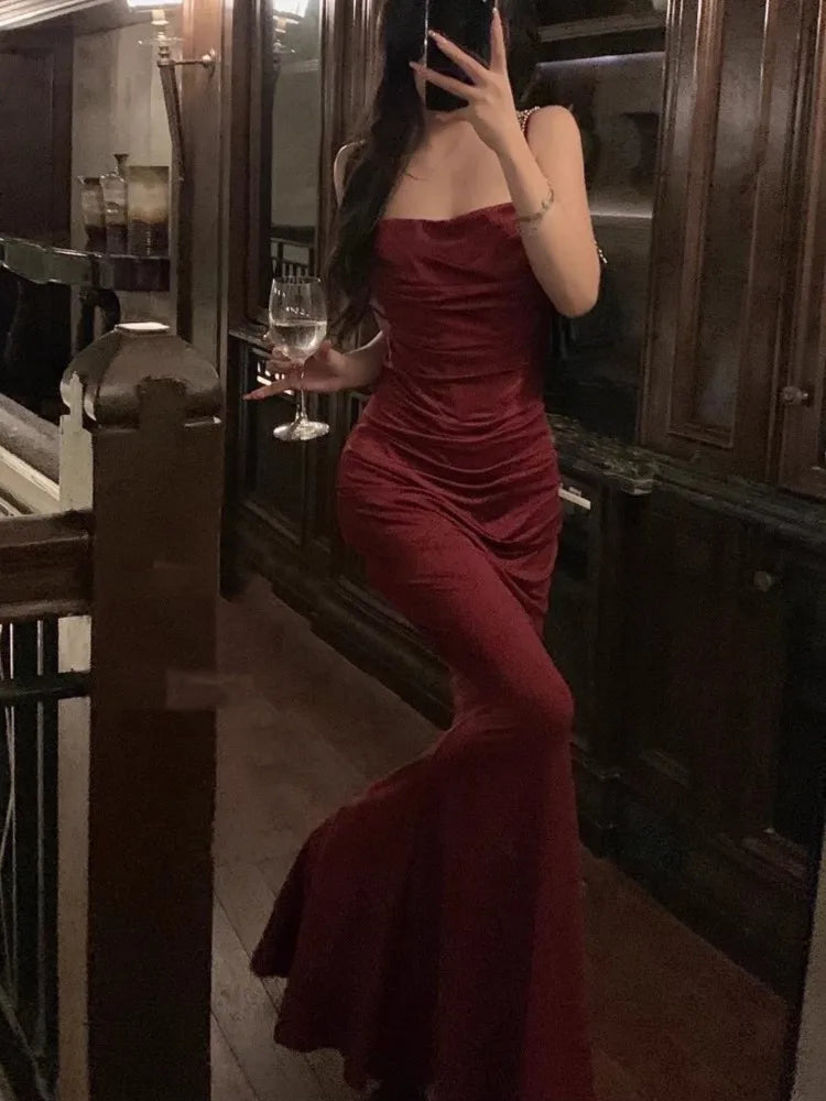Femme en robe de soirée rouge tenant un verre de vin, posant dans un intérieur élégant en bois sombre. Mode élégante, soirée chic.