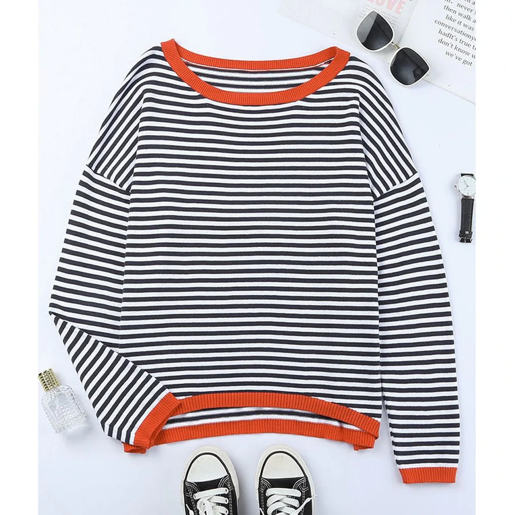 Pull rayé noir et blanc à manches longues, col et poignets orange, posé à plat avec lunettes de soleil et baskets noires en arrière-plan.