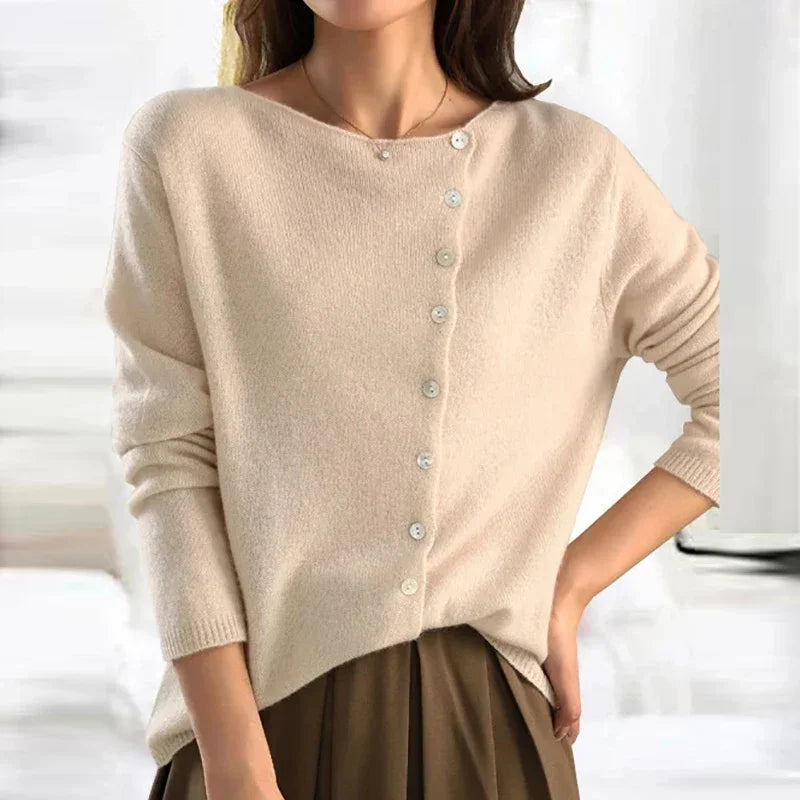 Femme portant un pull beige asymétrique avec boutons, manches longues, col bateau. Mode élégante, tendance automne-hiver, style décontracté chic.