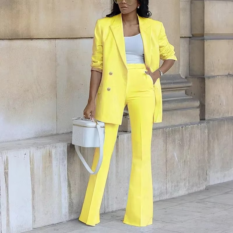Femme en costume jaune vif, blazer et pantalon évasé, tenant un sac blanc. Mode élégante, tendance printemps, look professionnel chic.