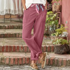 Pantalon rose décontracté pour femme avec ceinture foulard, poches avant, chaussures bateau marron, ambiance extérieure rustique.