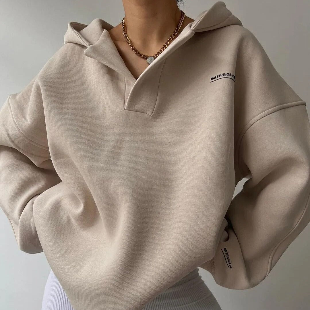 Femme portant un sweat à capuche beige élégant, col ouvert, chaîne dorée, style décontracté. Mode automne, tendance vêtements confortables.