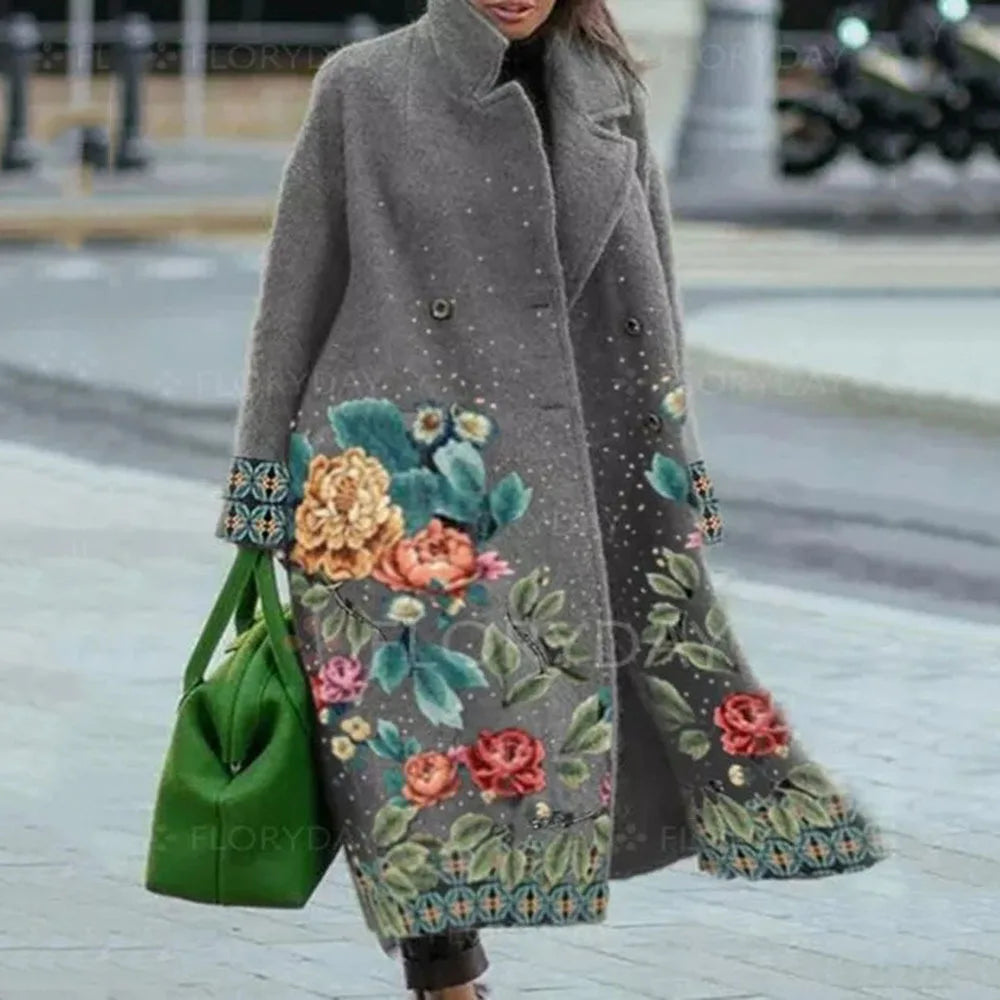 Femme portant un manteau gris à motifs floraux colorés, tenant un sac vert vif. Mode hiver élégante, tendance et chic en ville.
