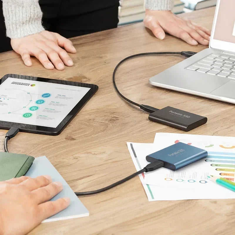 Deux disques SSD portables connectés à un ordinateur portable et une tablette sur un bureau en bois, illustrant le stockage externe rapide et efficace.