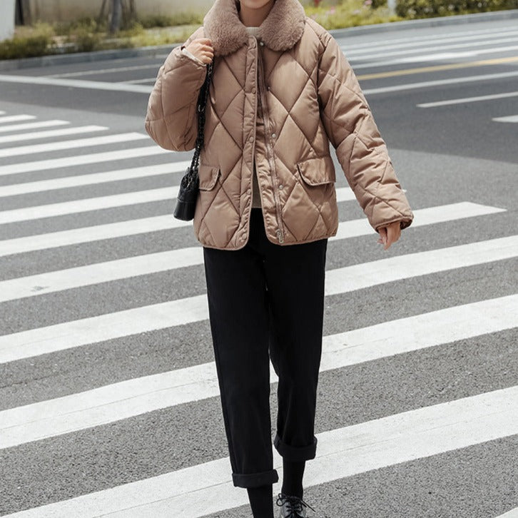 Personne portant une veste matelassée beige avec col en fourrure, traversant un passage piéton. Mode hiver, tenue décontractée, rue urbaine.