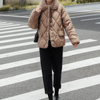 Personne portant une veste matelassée beige avec col en fourrure, traversant un passage piéton. Mode hiver, tenue décontractée, rue urbaine.