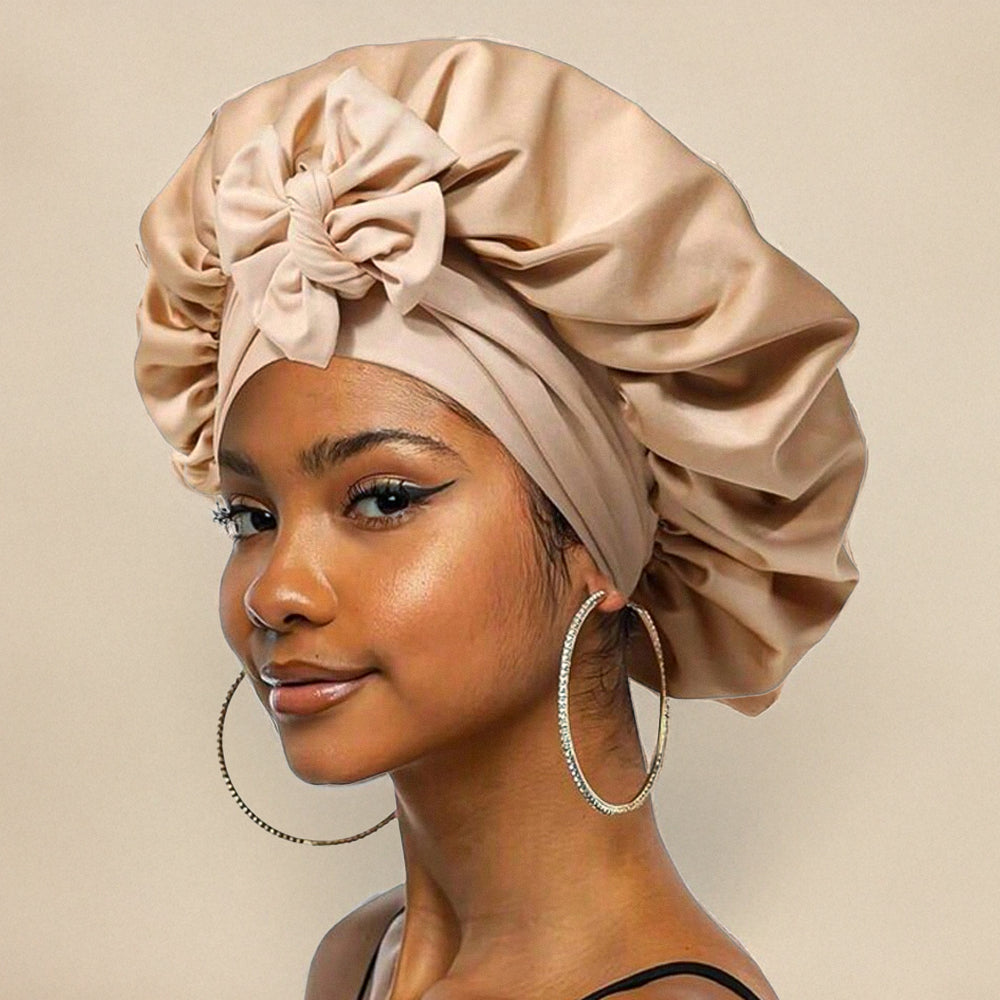 Jeune femme portant un bonnet en satin beige avec un nœud, boucles d'oreilles créoles argentées, maquillage subtil, fond beige. Mode, accessoires cheveux.