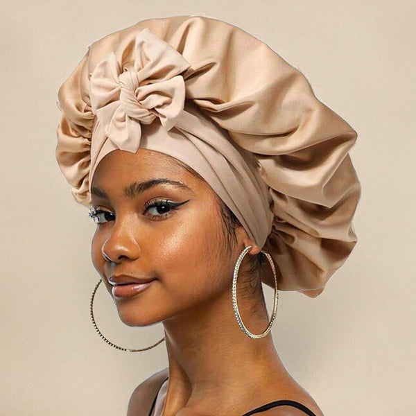 Jeune femme portant un bonnet en satin beige avec un nœud, boucles d'oreilles créoles argentées, maquillage subtil, fond beige. Mode, accessoires cheveux.
