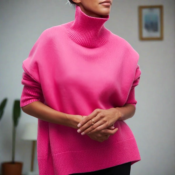 Femme portant un pull rose à col roulé, manches retroussées, dans un intérieur moderne. Mode automne-hiver, style décontracté et élégant.