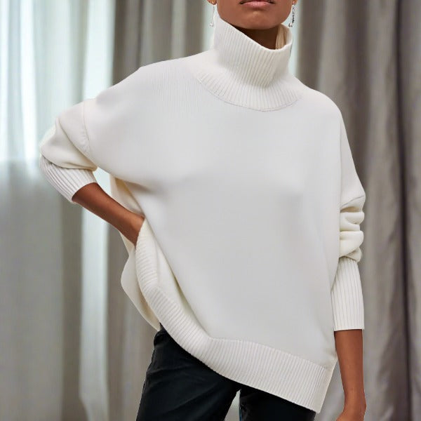 Femme portant un pull blanc à col roulé, manches longues, style décontracté, devant un rideau gris. Mode automne-hiver, tendance élégante.