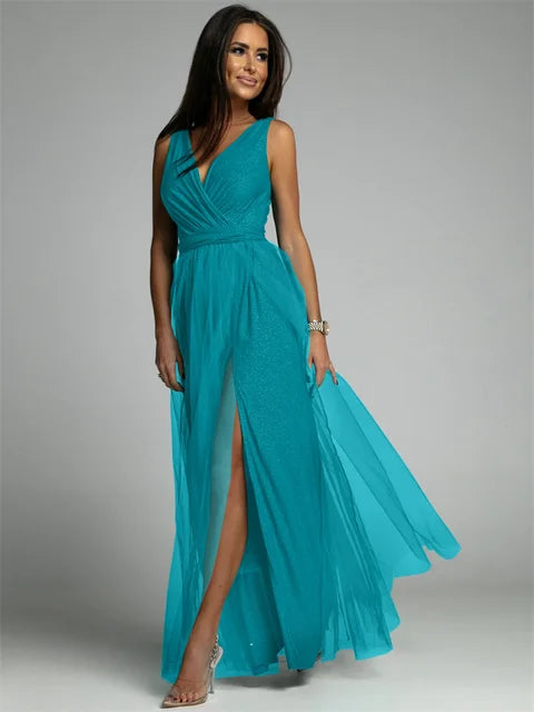 Femme portant une robe longue turquoise élégante avec décolleté en V et fente haute, posant sur fond gris. Mode féminine, tenue de soirée chic.