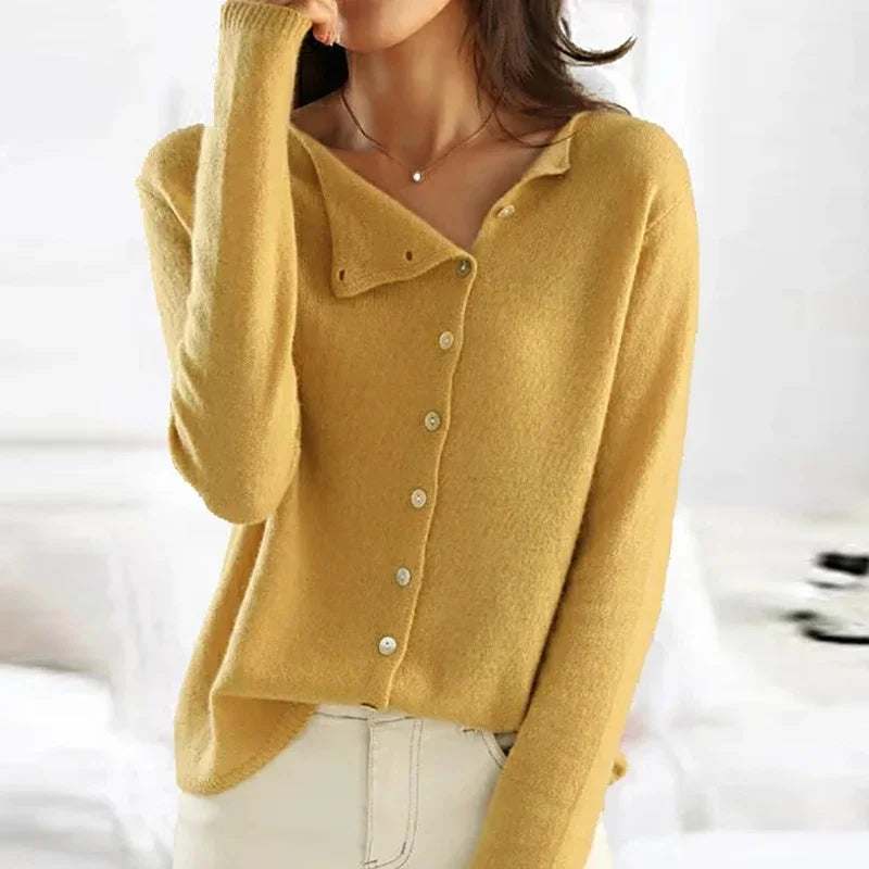 Femme portant un pull jaune en cachemire avec boutons, style décontracté chic, mode automne-hiver, intérieur lumineux.