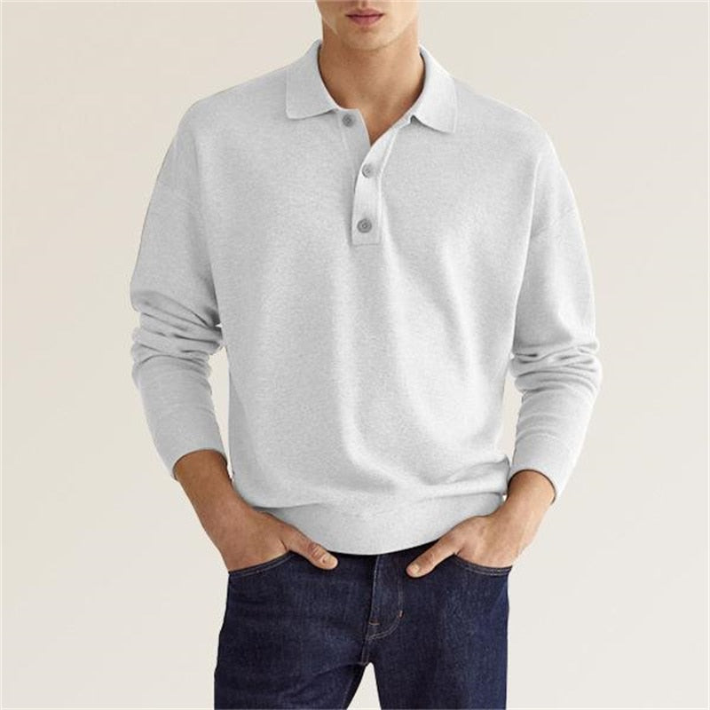Homme portant un pull gris à col polo et manches longues, associé à un jean bleu foncé. Mode décontractée, style élégant et moderne.