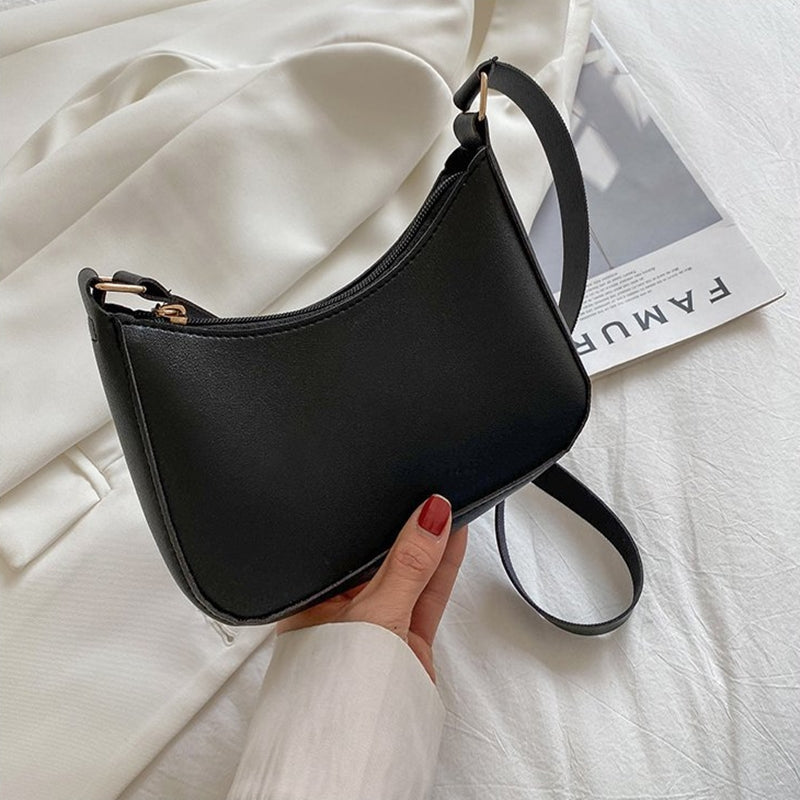 Sac à main noir élégant en cuir, tenu par une main avec vernis rouge, posé sur un fond blanc avec magazine. Accessoire mode tendance pour femme.