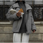 Personne portant une veste grise en laine, tenant un croissant, devant une balustrade en fer forgé. Mode hiver, style urbain, Paris.