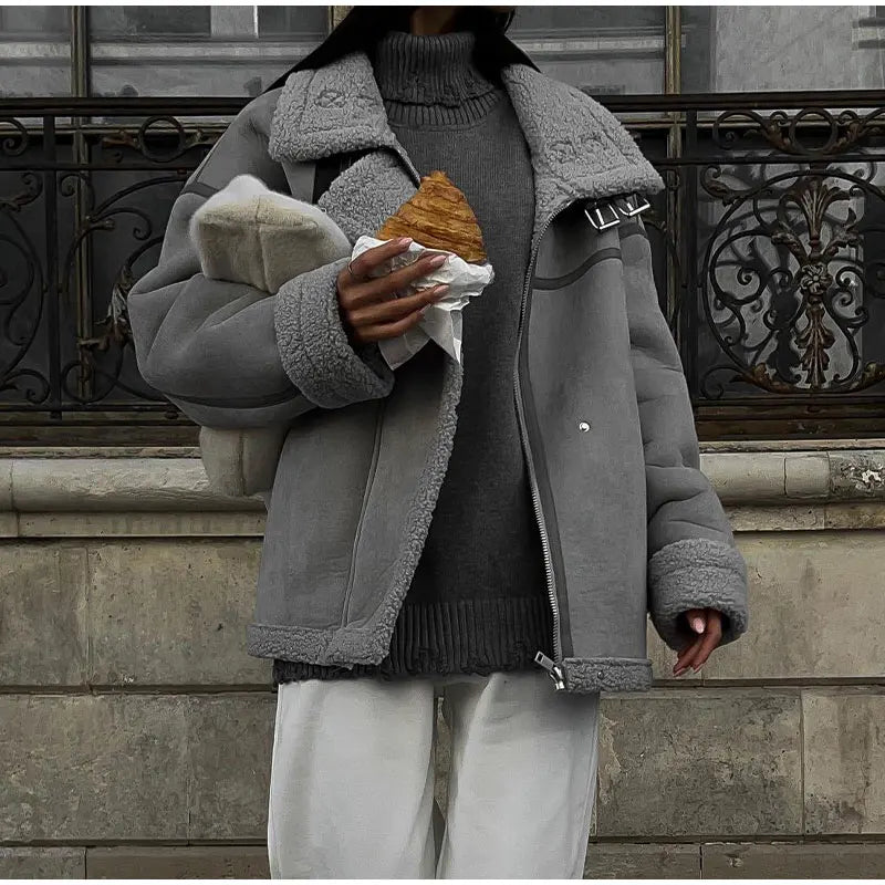 Personne portant une veste grise en laine, tenant un croissant, devant une balustrade en fer forgé. Mode hiver, style urbain, Paris.
