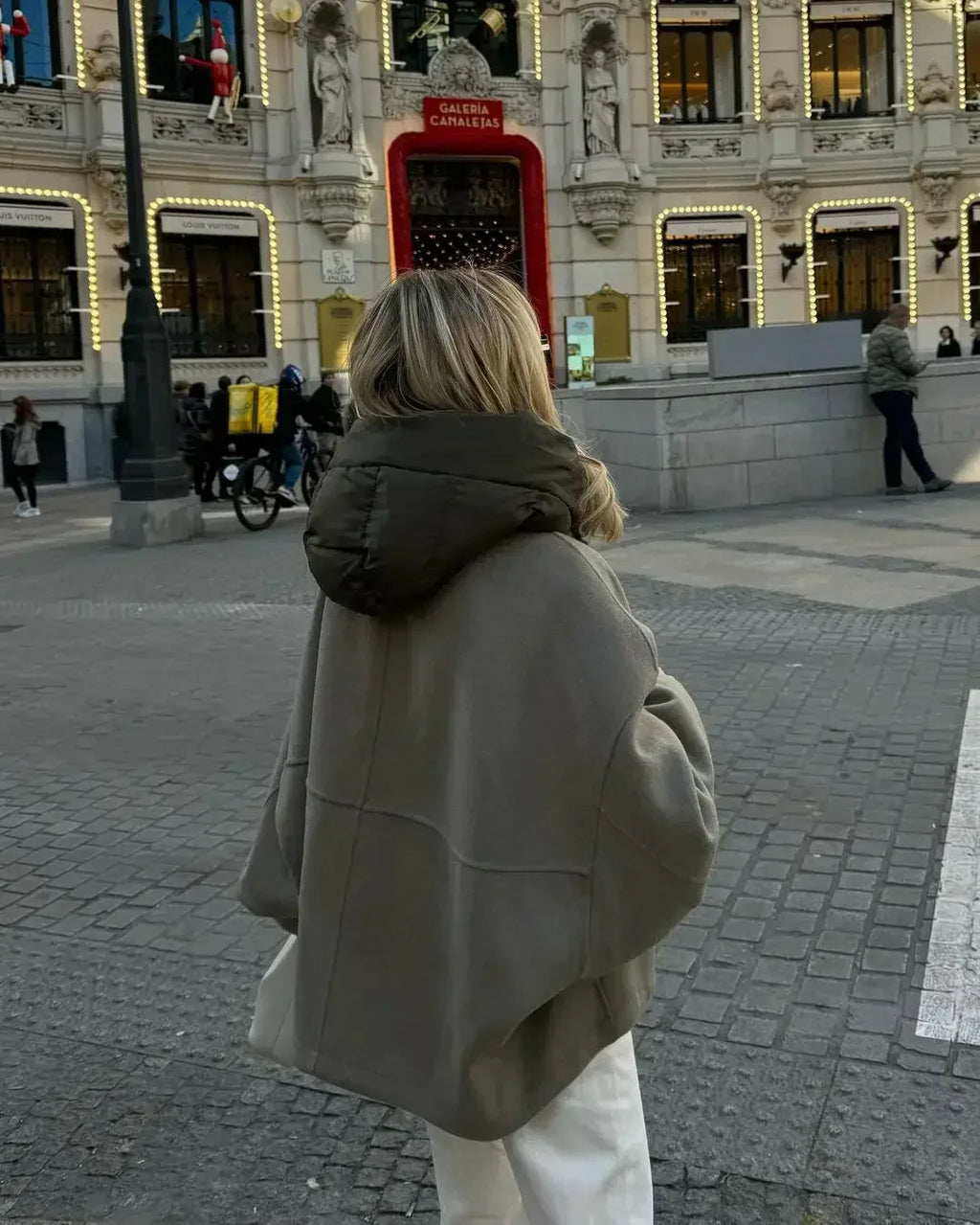 Femme en manteau gris devant le théâtre Callao à Madrid, Espagne, avec décorations lumineuses et passants. Scène urbaine animée en hiver.