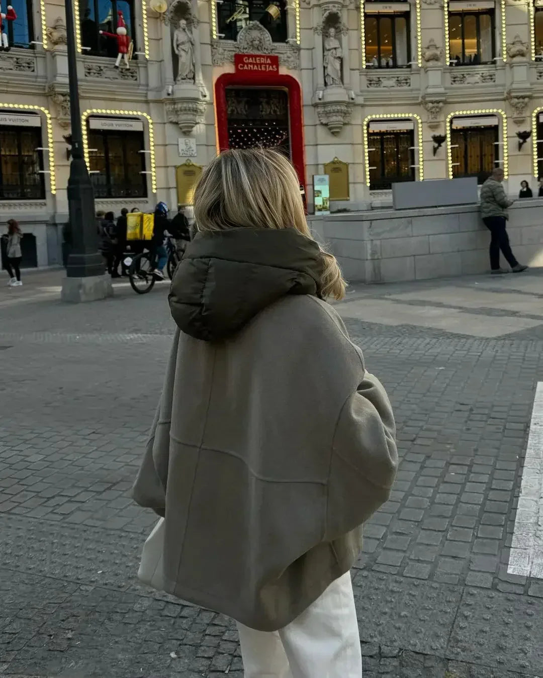Femme en manteau gris devant le théâtre Callao à Madrid, Espagne, avec décorations lumineuses et passants. Scène urbaine animée en hiver.