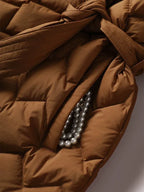 Veste matelassée marron avec poche ouverte révélant un collier de perles grises. Mode automne, style élégant, détails accessoires.
