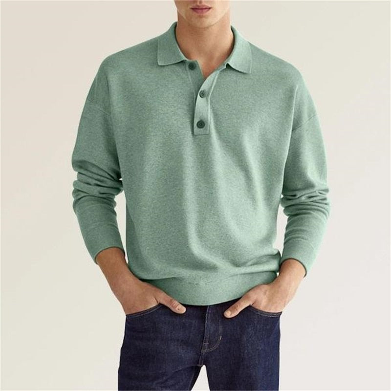 Homme portant un pull polo vert, manches longues, col boutonné, associé à un jean bleu. Mode masculine décontractée, style élégant et moderne.