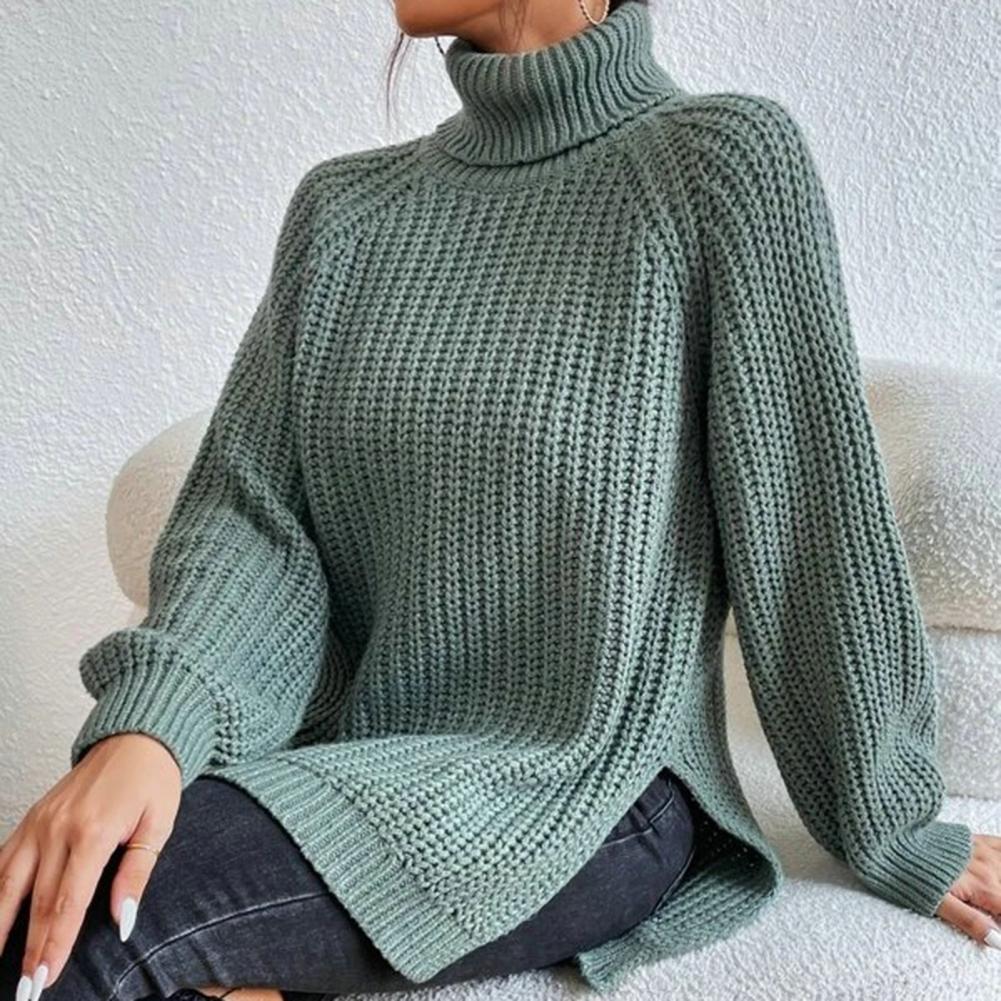 Femme portant un pull en maille vert à col roulé, manches longues, assise sur un canapé blanc. Mode automne-hiver, style décontracté et élégant.
