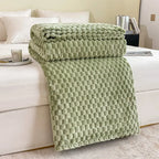 Couverture en peluche verte texturée sur un lit blanc, avec oreillers blancs en arrière-plan. Décoration intérieure moderne et confortable.