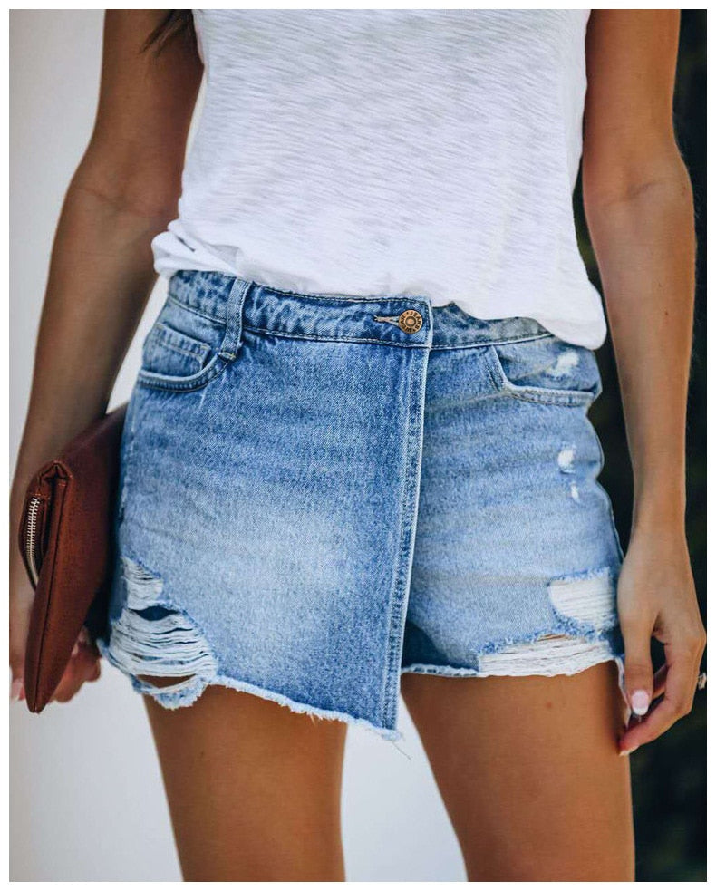 Femme portant un short en jean déchiré avec un t-shirt blanc, tenant une pochette marron. Mode estivale, style décontracté, tendance denim.