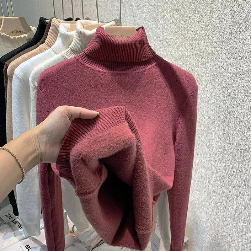 Pulls à col roulé en laine pour femme, disponibles en plusieurs couleurs, exposés sur un portant. Main tenant un pull rose doux et chaud.