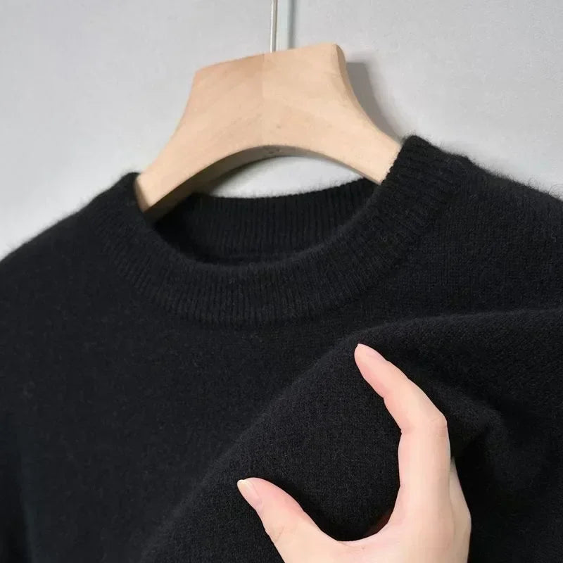 Pull noir en laine sur cintre en bois, gros plan. Texture douce et col rond, idéal pour mode automne-hiver. Vêtement chaud et élégant.