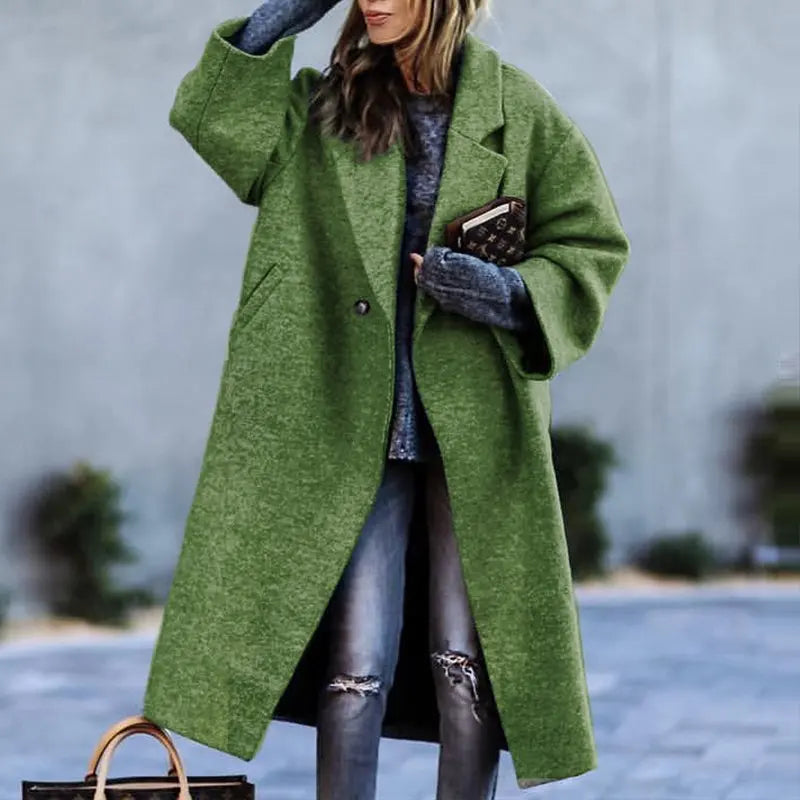 Femme portant un manteau vert oversize, jeans déchirés et pull gris, tenant un livre et un sac à main. Mode automne-hiver, style décontracté.