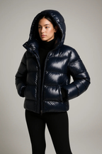Femme portant une doudoune noire brillante avec capuche, style hiver, mode féminine, vêtement chaud, tendance, sur fond gris.