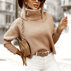 Femme élégante en pull beige à col roulé, sac à chaîne dorée, chapeau marron, lunettes de soleil, tenue automnale chic, mode urbaine tendance.