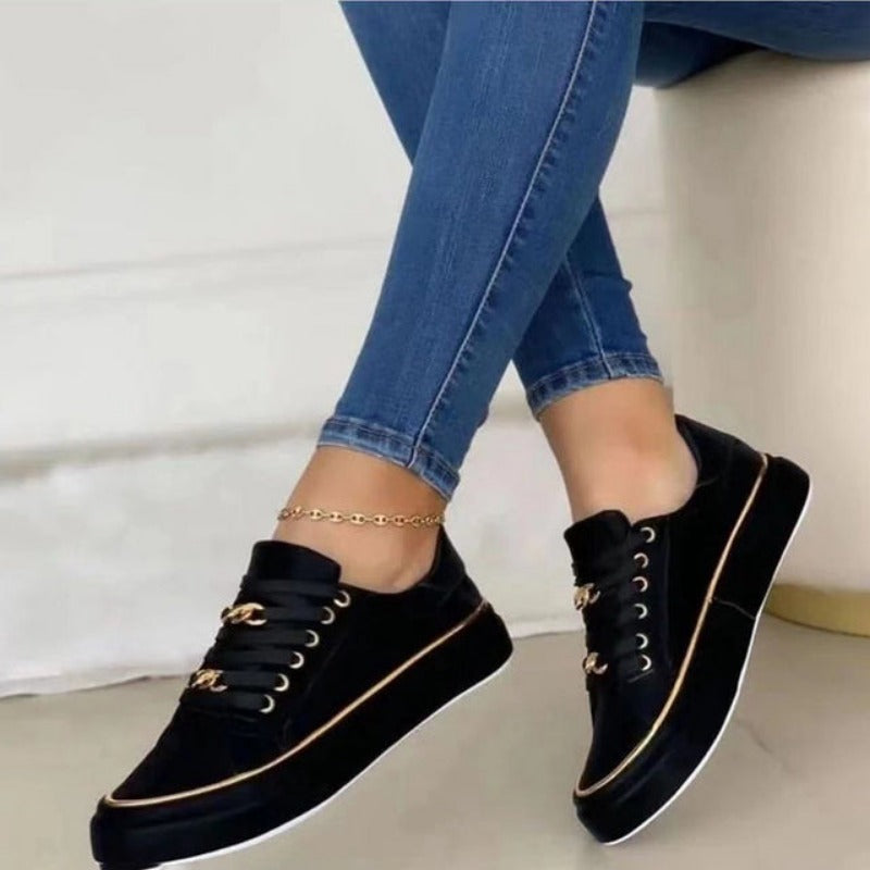 Chaussures noires élégantes avec lacets dorés portées avec un jean bleu. Sneakers tendance pour femme, style décontracté et moderne.