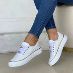 Chaussures blanches élégantes pour femmes avec détails dorés, portées avec un jean ajusté. Sneakers tendance, mode féminine, style décontracté.