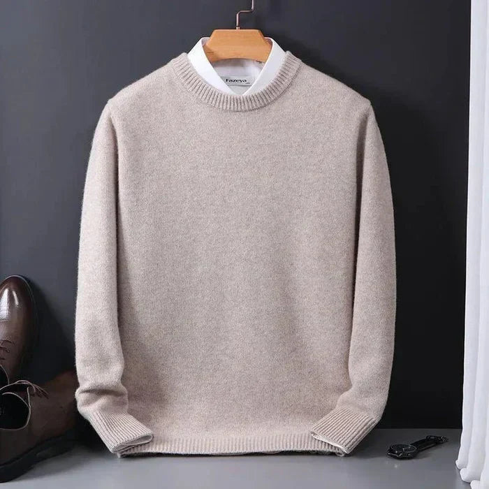 Pull beige en laine sur cintre, chemise blanche en dessous, chaussures marron et montre noire à côté. Mode homme élégante et classique.