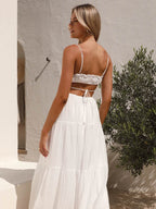 Jeune femme en robe d'été blanche dos nu, debout près d'un mur blanc et d'un olivier, style bohème chic, mode estivale tendance.