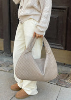 Personne portant un sac à main tissé beige, pantalon blanc et chaussures marron, devant une porte en bois sombre. Mode automne, style décontracté.