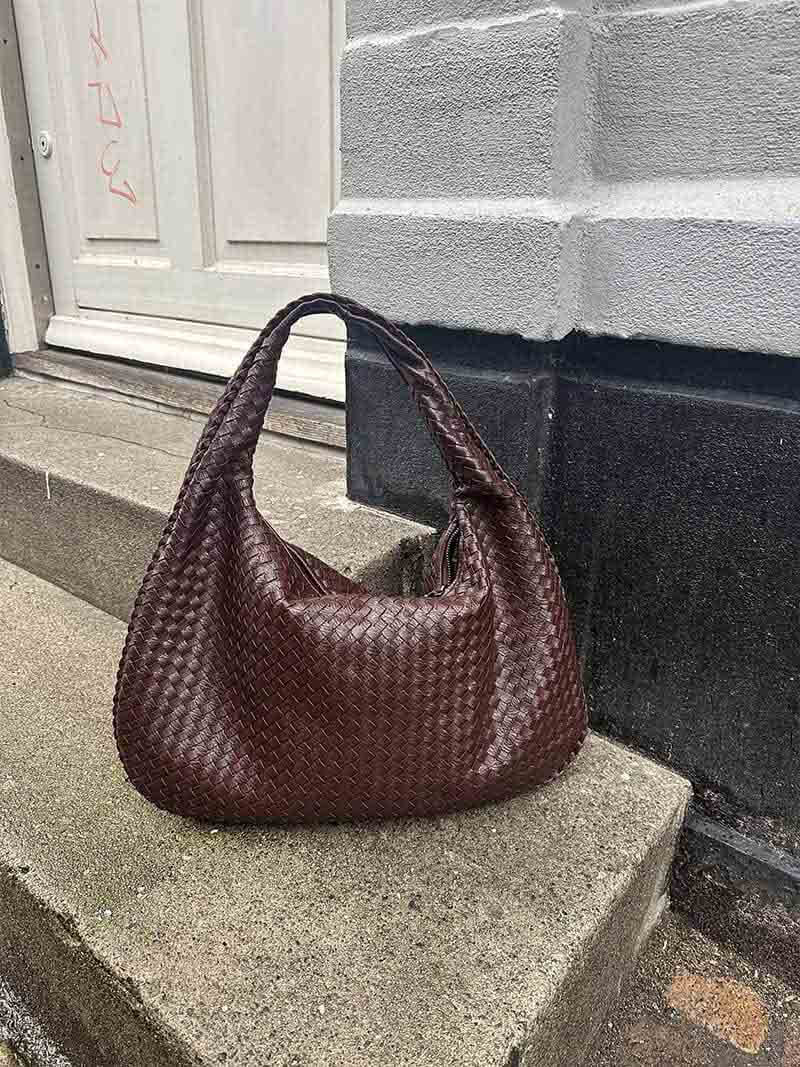 Sac à main en cuir tressé marron posé sur des marches en béton devant une porte blanche. Accessoire mode élégant et tendance.