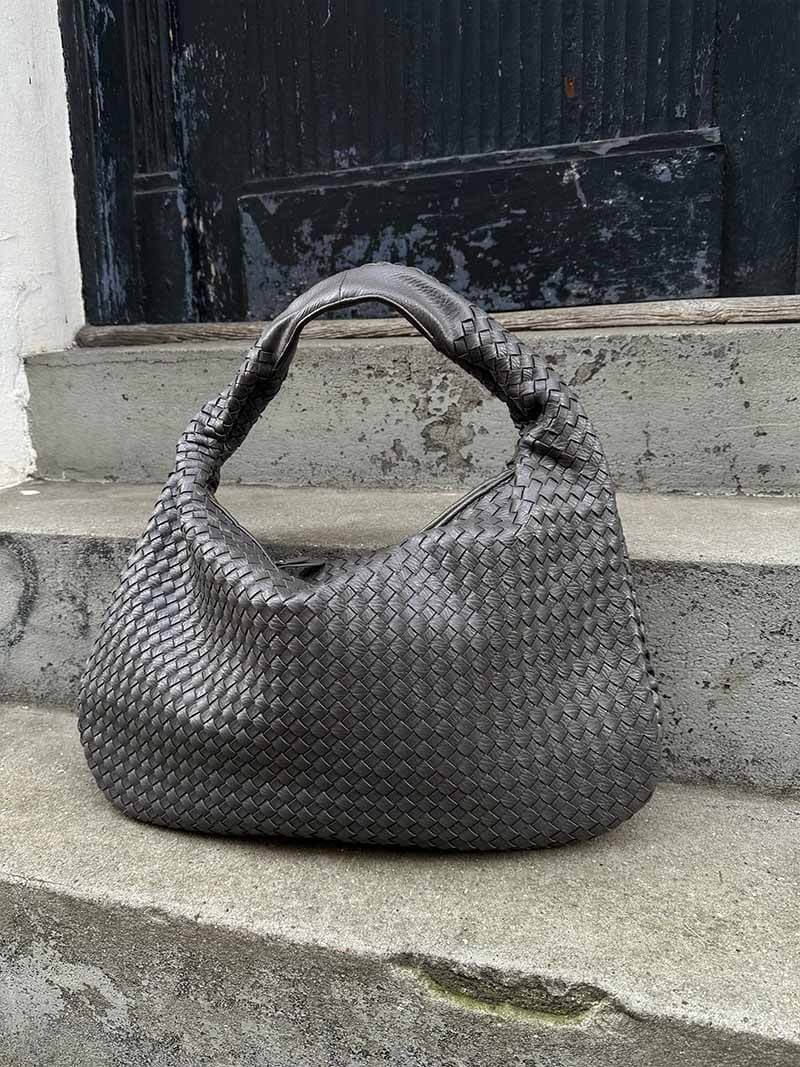 Sac à main en cuir tressé gris sur marches en béton, design élégant et moderne, accessoire de mode tendance pour femmes.