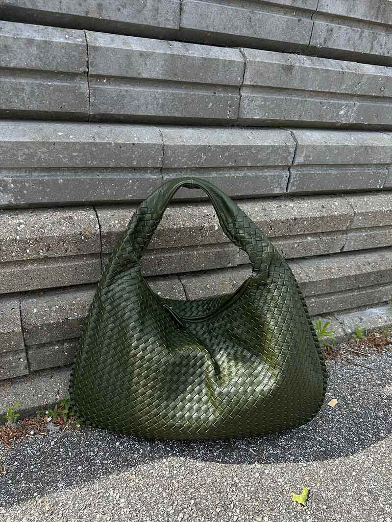 Sac à main vert tressé en cuir, posé contre un mur de briques grises. Accessoire de mode élégant et tendance, idéal pour un look chic.