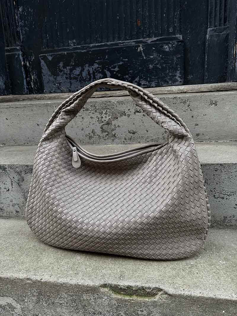 Sac à main en cuir tressé gris sur des marches en pierre. Accessoire de mode élégant, tendance, idéal pour un look chic et moderne.
