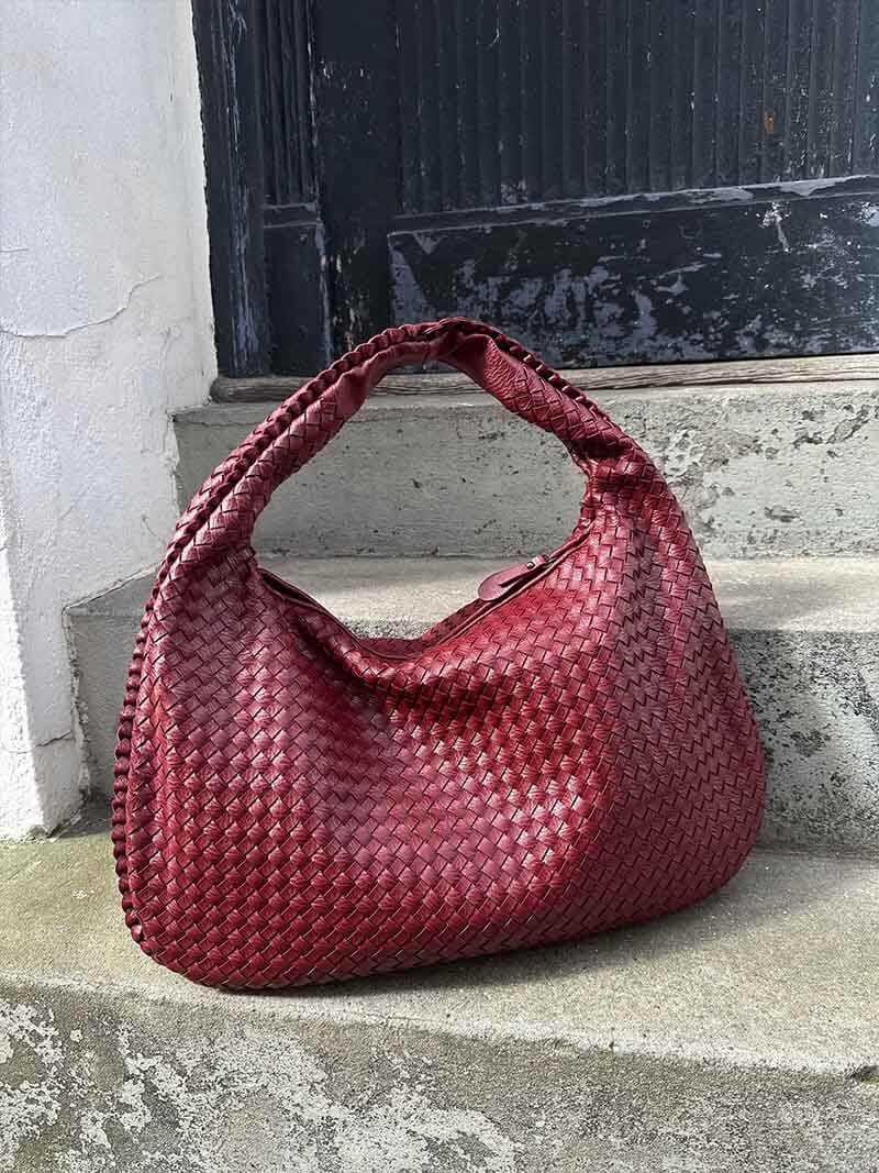 Sac à main en cuir tressé rouge bordeaux sur des marches en béton. Accessoire mode élégant, tendance et chic pour femme.